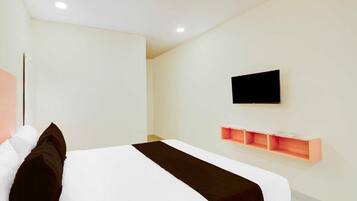 Una habitación de hotel moderna con una cama grande, televisor montado y estanterías integradas.