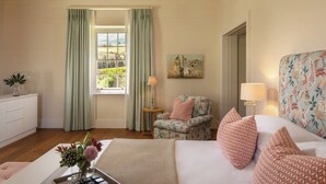 A well-lit room with a bed, a floral armchair, a side table with a lamp, and a painting on the wall. - Brookdale Estate - Manor House (Cape Town)