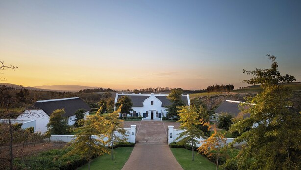 A white building with a central entrance, surrounded by greenery and a clear sky. - Brookdale Estate - Manor House (Cape Town)