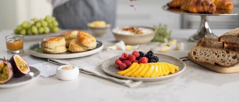 A breakfast setting with pastries, fruits, and a glass of juice on a table.