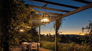 An outdoor patio with a wooden deck, a table, and chairs, surrounded by lush greenery and a view of distant hills. - Brookdale Estate - Manor House (Cape Town)