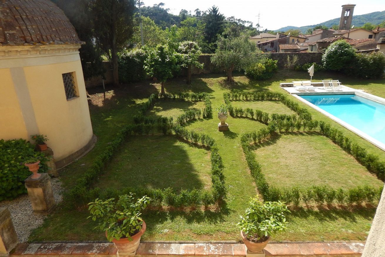 A garden with a swimming pool, a small building, and a view of a village.