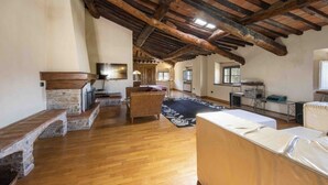 Ein großzügiges Loft mit freiliegenden Holzbalken, einem Kamin, einem großen Fenster und einer gemütlichen Sitzecke.