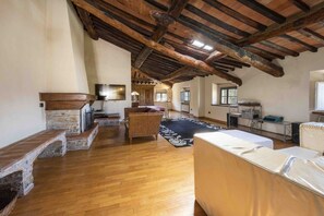 A spacious loft with exposed wooden beams, a fireplace, a large window, and a cozy seating area.