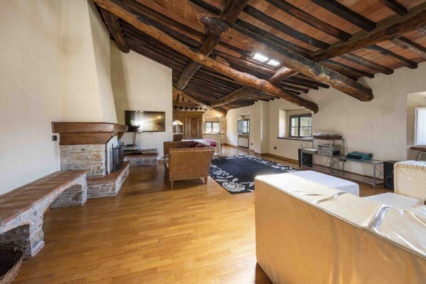 Un loft espacioso con vigas de madera a la vista, chimenea, un gran ventanal y una zona de estar acogedora.