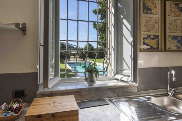 A kitchen with a large window overlooking a pool, a wooden box labeled 'SAN FELICE,' and a marble countertop.