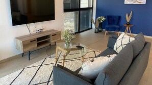Una sala de estar moderna con un televisor de pantalla plana, un mueble de madera para entretenimiento, una mesa de centro de vidrio, un sofá gris y una pared de acento azul.