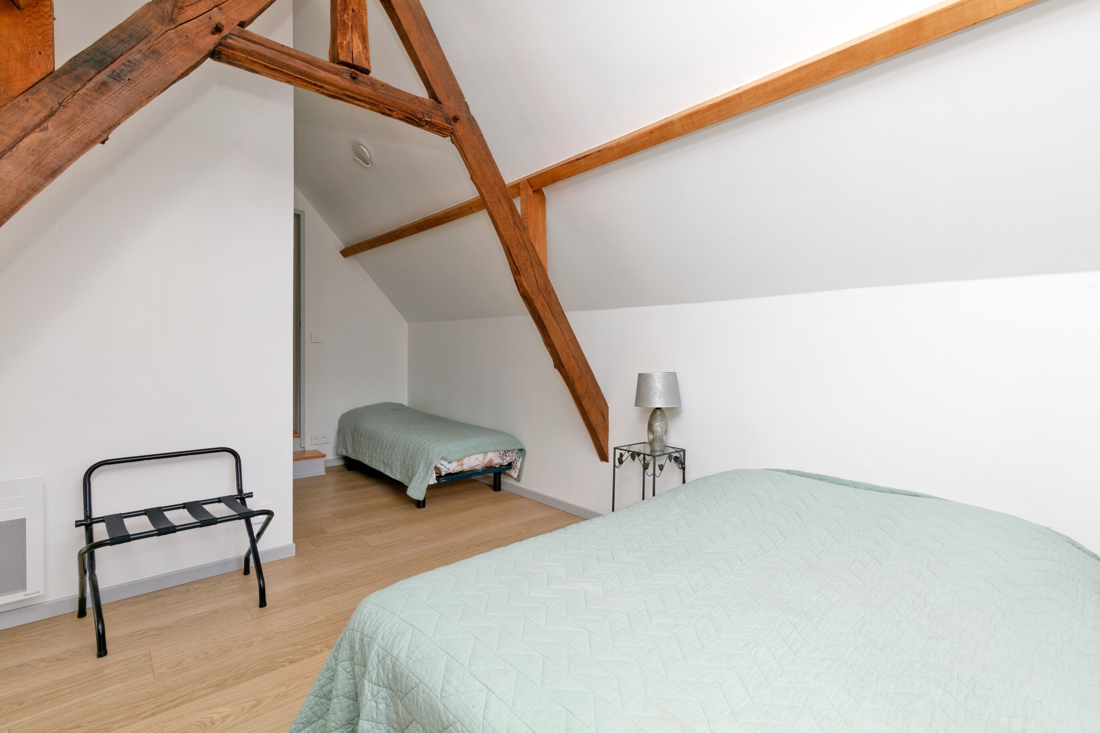 Een slaapkamer met een schuine plafond, een bed, een bankje en een nachtkastje.