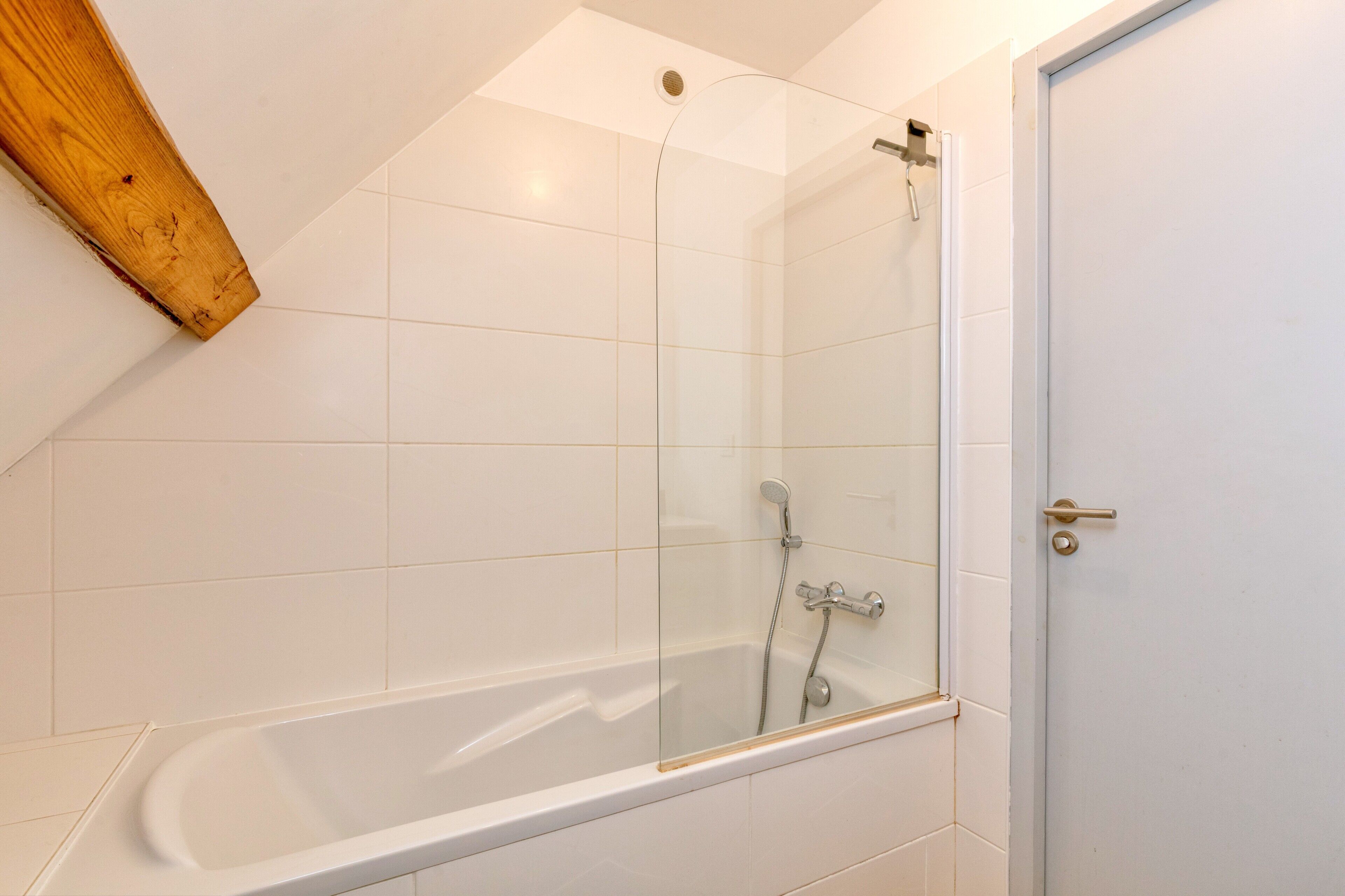 Ein modernes Badezimmer mit einer gläsernen Dusche, weißen Fliesen und einem Holzbalken.