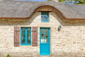 Ein Gebäude aus Stein mit einem Strohdach, einer Holztür und einem Fenster mit Fensterläden.