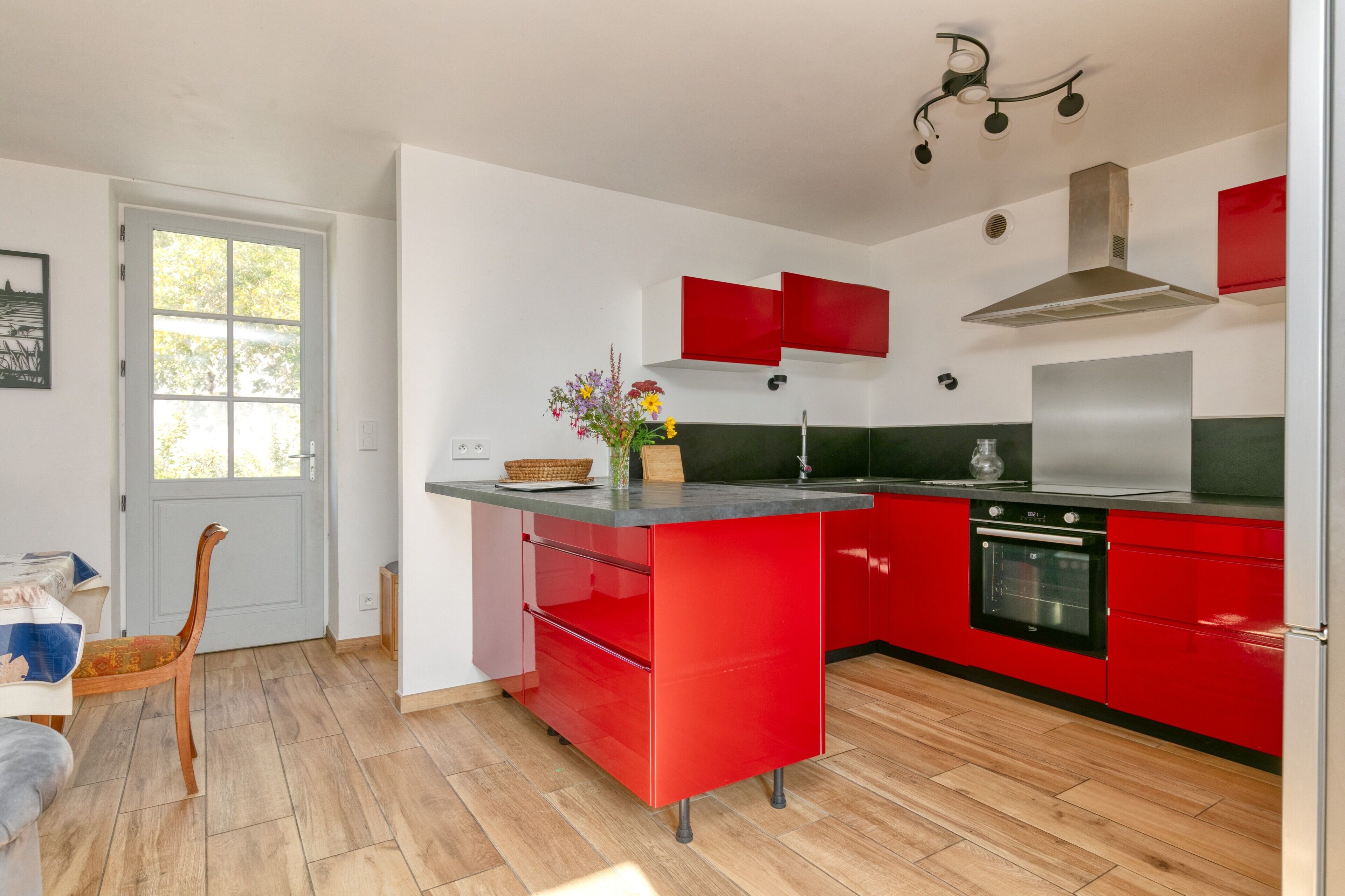 A modern kitchen with red cabinetry, a black stove, and a window with a view.
