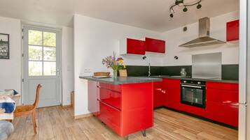 A modern kitchen with red cabinetry, a black stove, and a window with a view.