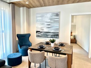 Ein Essbereich mit einem Tisch für vier Personen, einem blauen Sessel und einem großen abstrakten Gemälde an der Wand.
