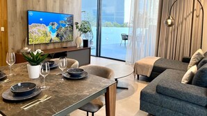 Ein modernes Wohnzimmer mit Essbereich, einem Flachbildfernseher und einem großen Fenster mit Blick ins Freie.