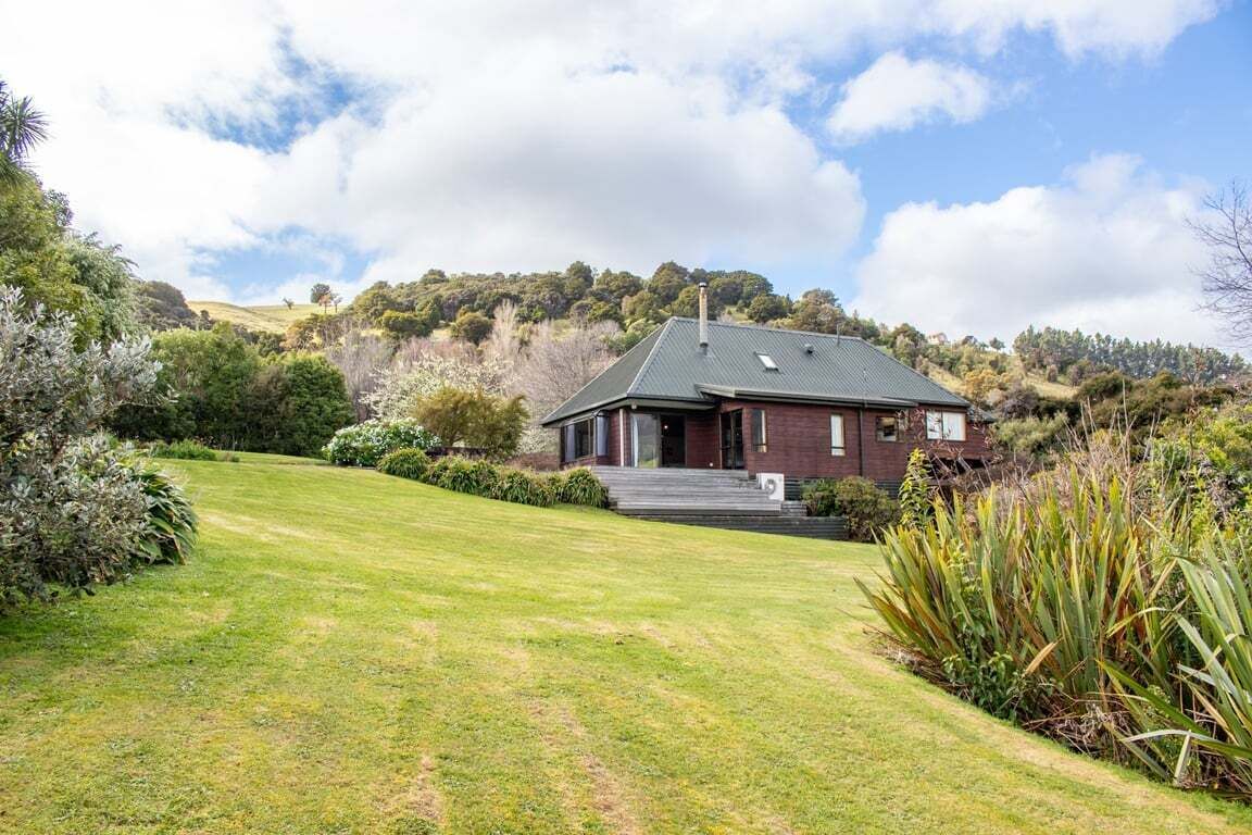 A house with a sloped roof, surrounded by a well-maintained lawn and various shrubs.