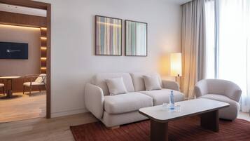 Una moderna camera d'hotel con divano, poltrone, tavolino, televisore e opere d'arte alle pareti.