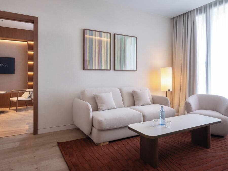 Una moderna camera d'hotel con divano, poltrone, tavolino, televisore e opere d'arte alle pareti.