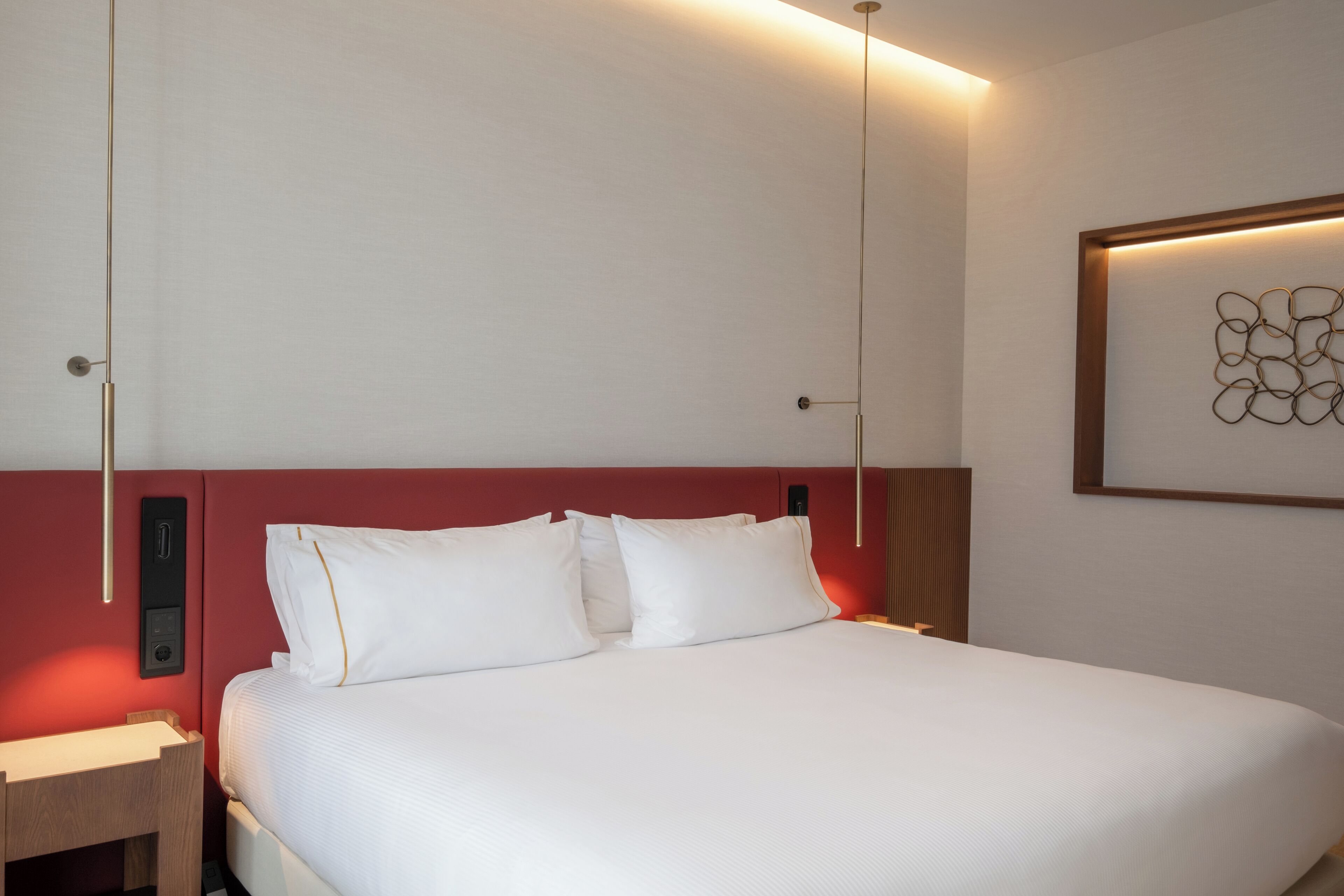 A hotel room with a bed, bedside tables, a wall-mounted artwork, and a red accent wall.