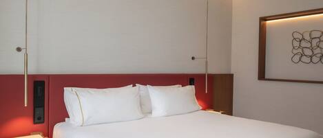A hotel room with a bed, bedside tables, a wall-mounted artwork, and a red accent wall.