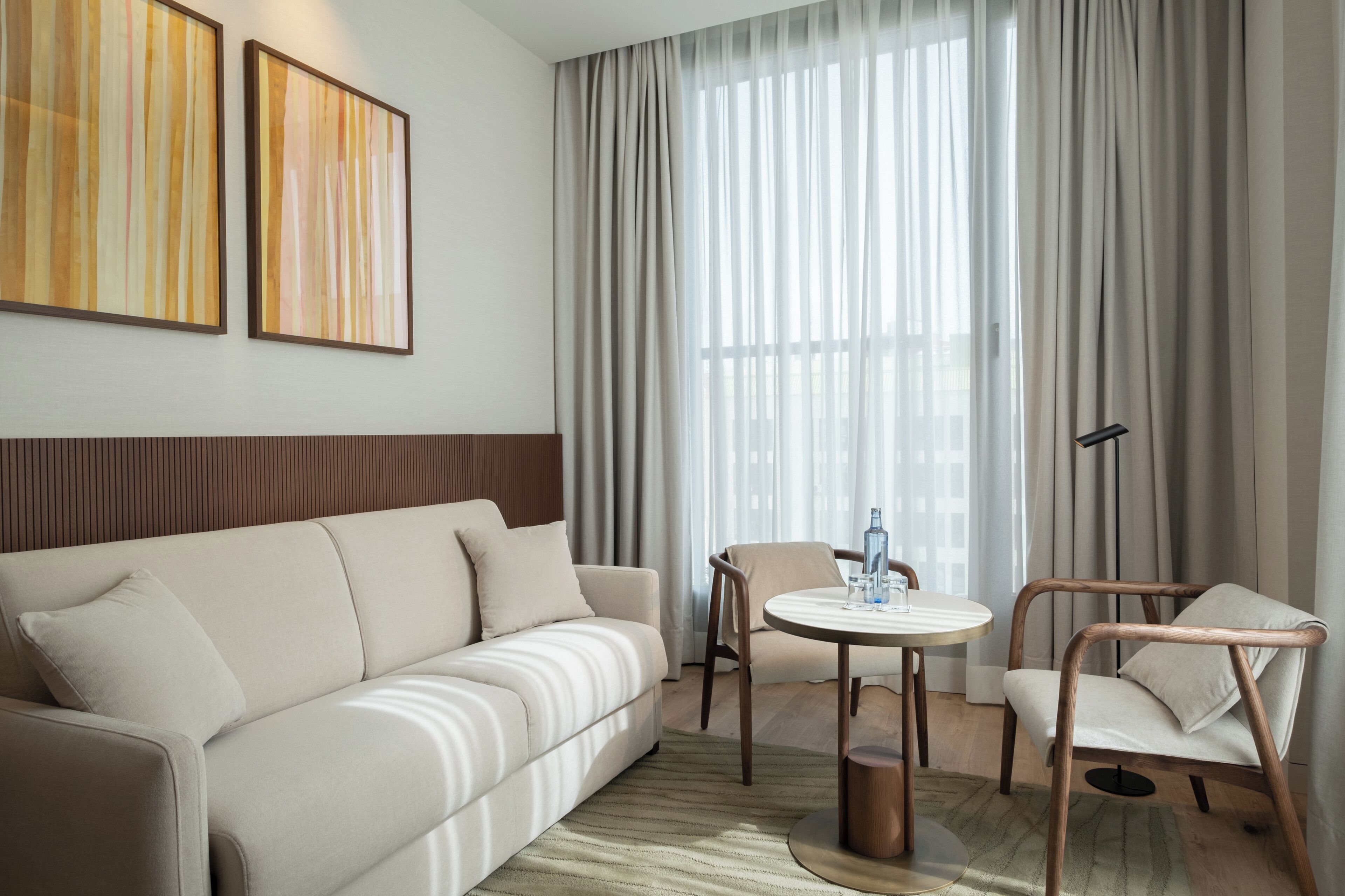 A hotel room with a sofa, a round table, a chair, and a floor lamp.