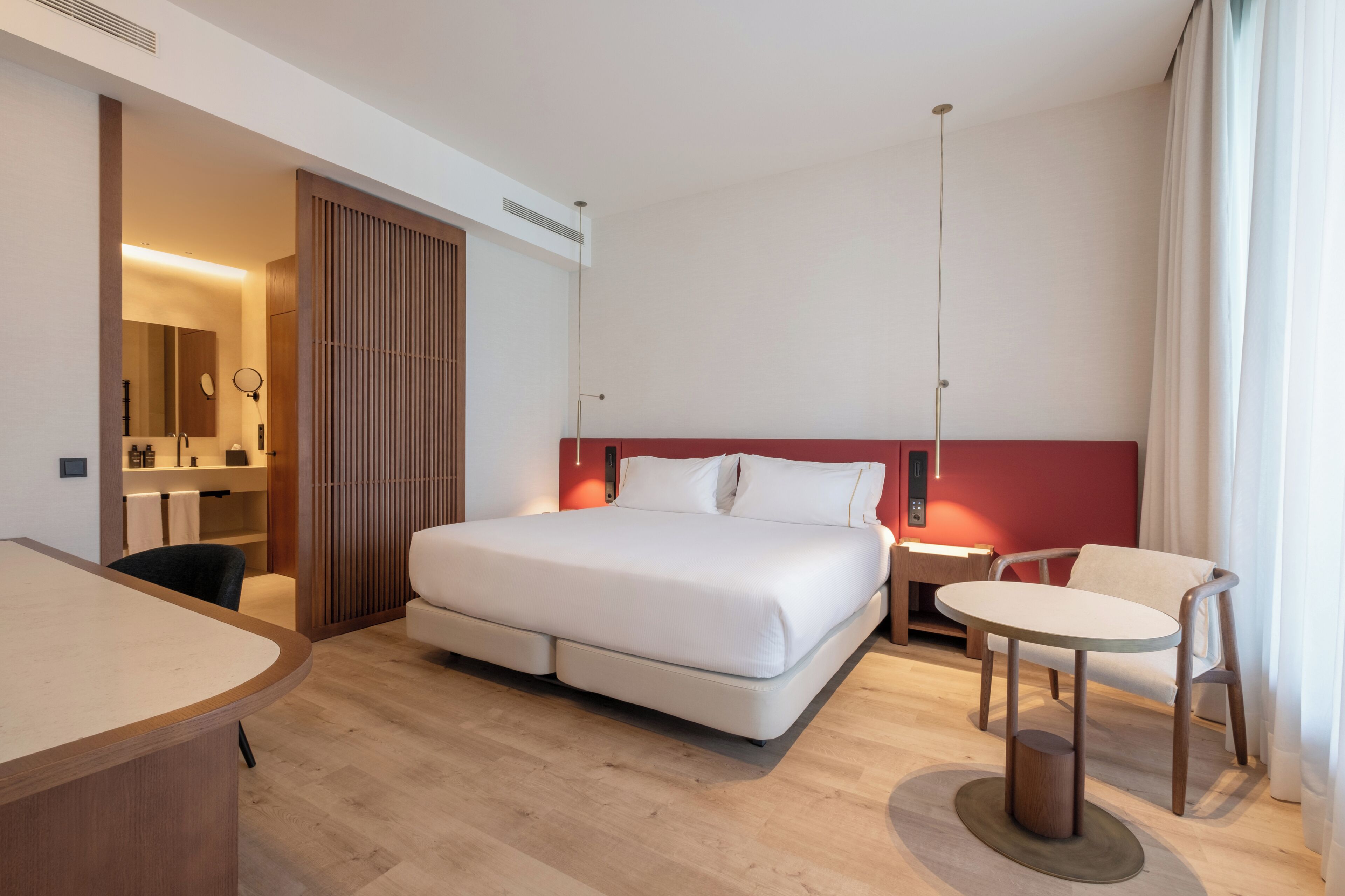 Moderni hotellihuone, jossa on suuri sänky, työpöytä, tuoli ja pieni pöytä.