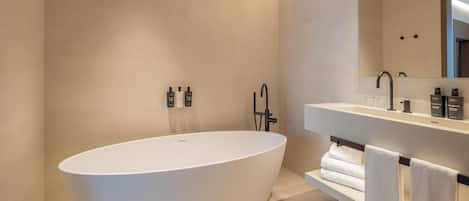 A modern bathroom with a freestanding bathtub, a large mirror, and a vanity with toiletries.