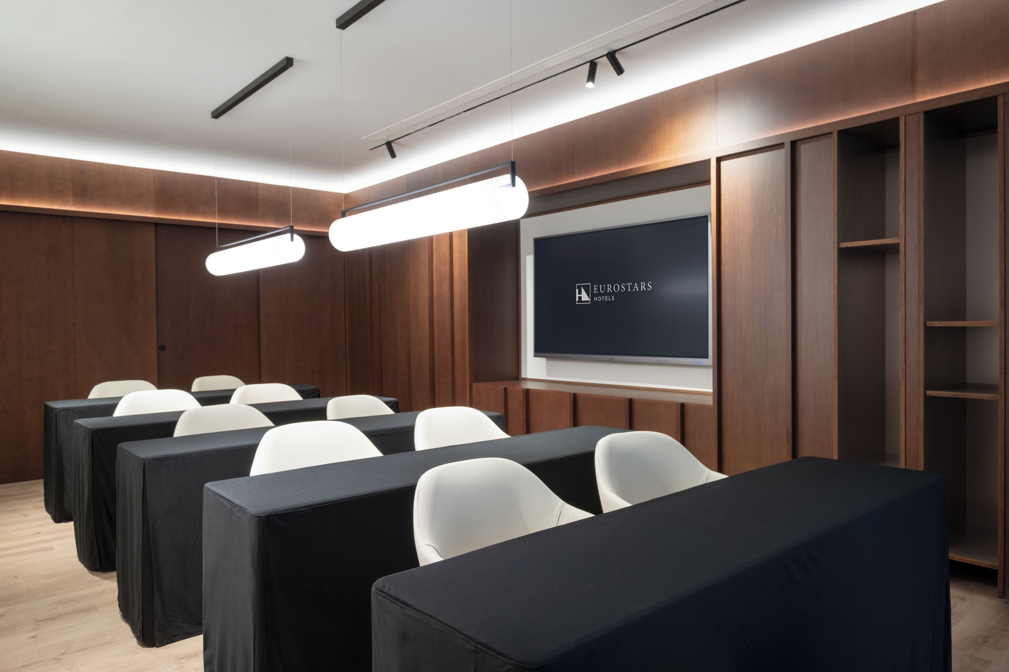 A conference room with rows of white chairs, a large screen, and wooden paneling.