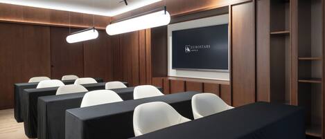A conference room with rows of white chairs, a large screen, and wooden paneling.