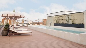 Zona de piscina al terrat amb gandules, una piscina i vista a edificis de la ciutat.