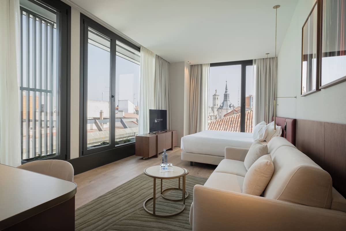 Une chambre d’hôtel équipée d’un lit, d’une télévision, d’un bureau et offrant une vue sur le paysage urbain.