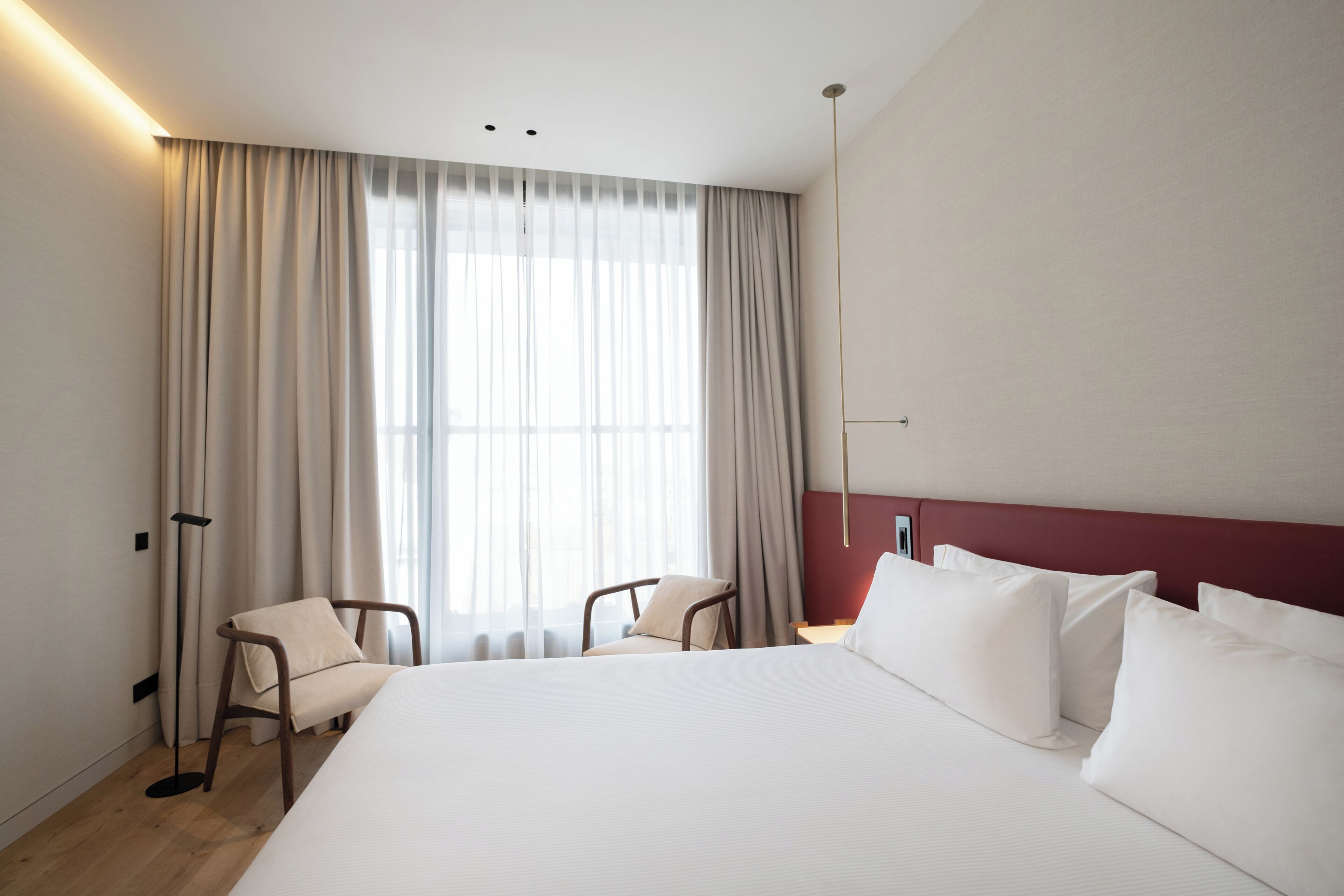 Habitación de hotel con una cama grande, dos sillas, una lámpara de pie y una ventana con cortinas.