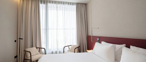 Habitación de hotel con una cama grande, dos sillas, una lámpara de pie y una ventana con cortinas.
