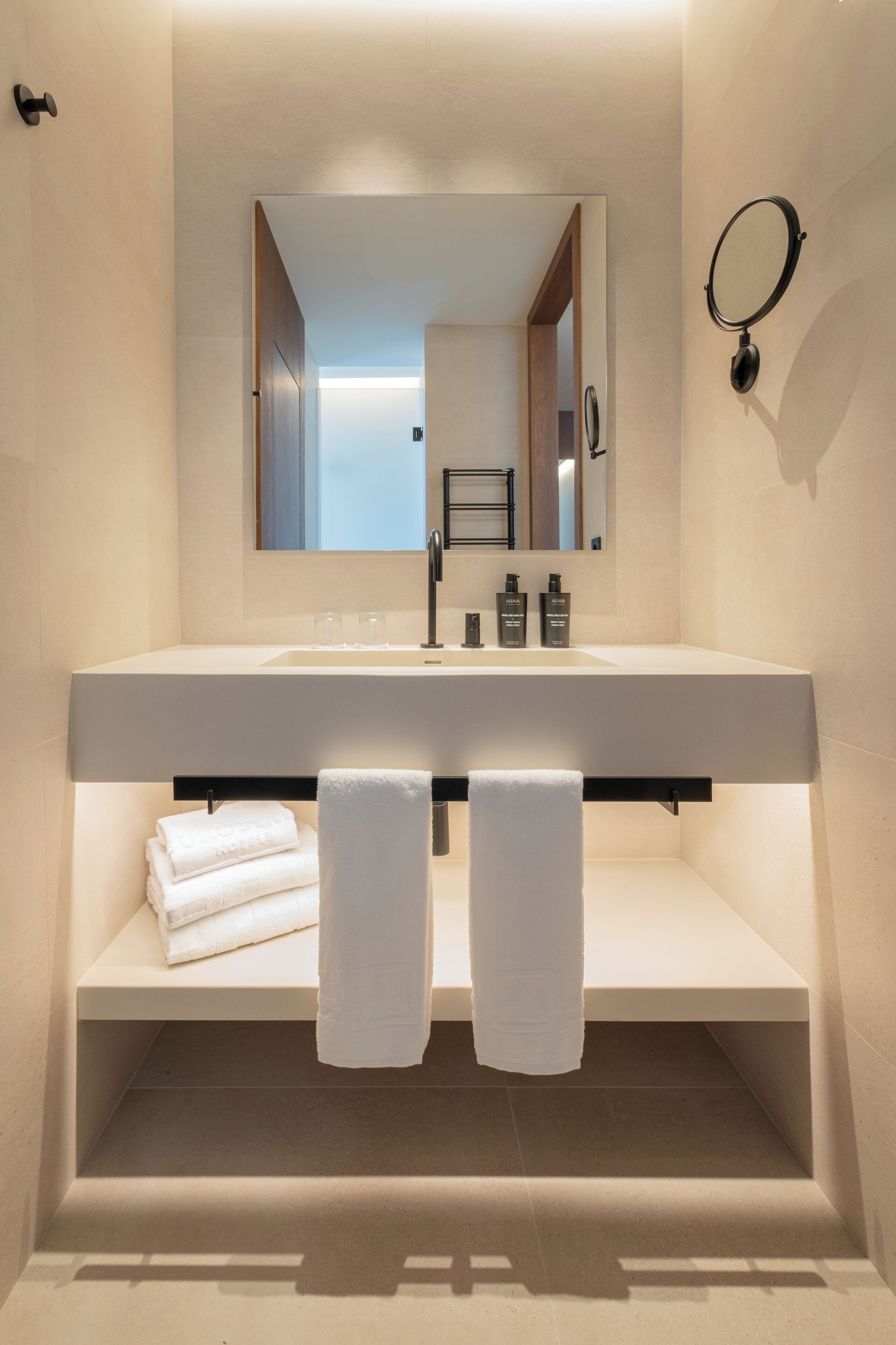 Un baño moderno con un espejo grande, un lavabo blanco y dos toallas en un estante.