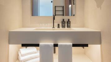 Un baño moderno con un espejo grande, un lavabo blanco y dos toallas en un estante.