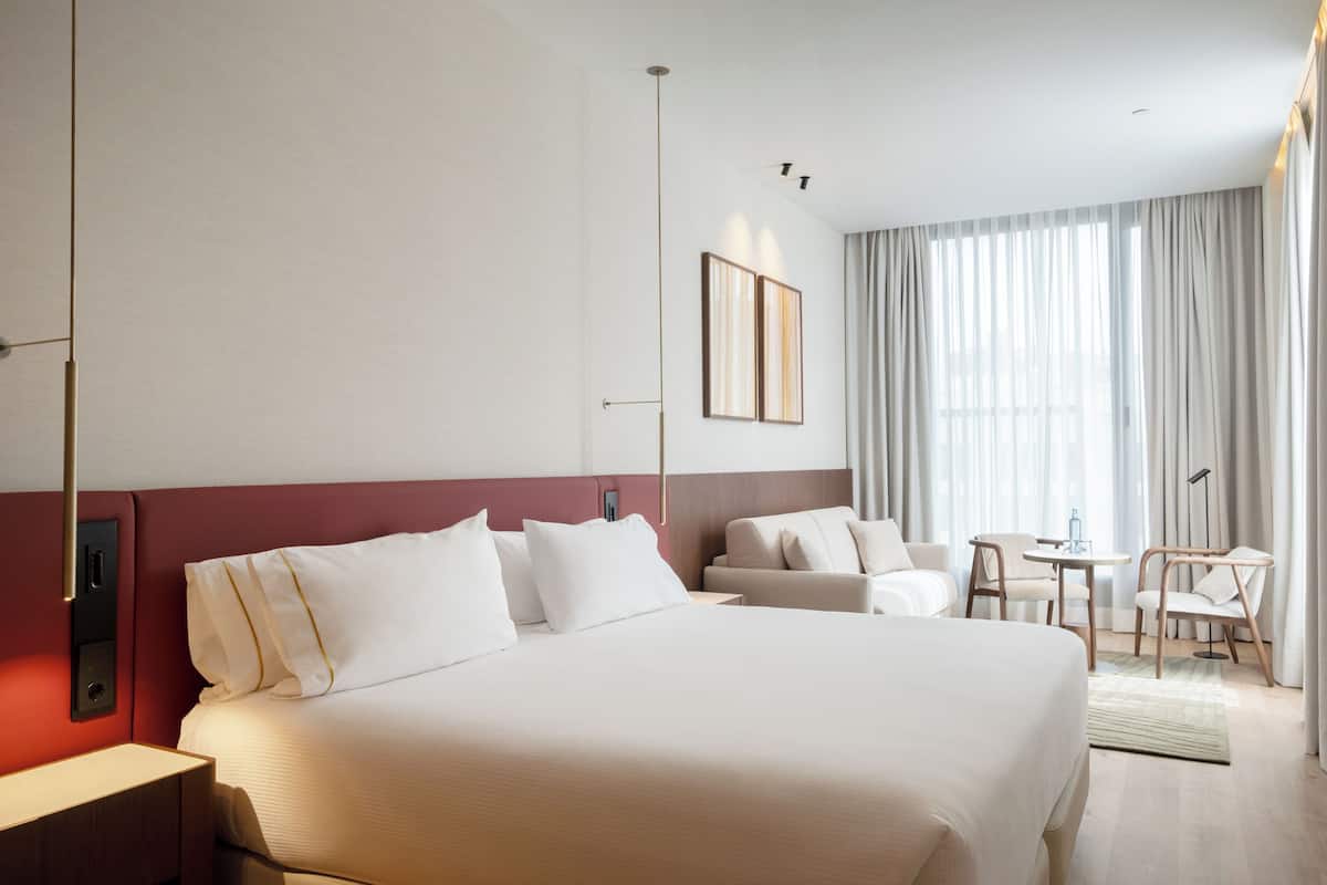 Une chambre d’hôtel avec un grand lit, un bureau, une chaise et une fenêtre avec des rideaux.