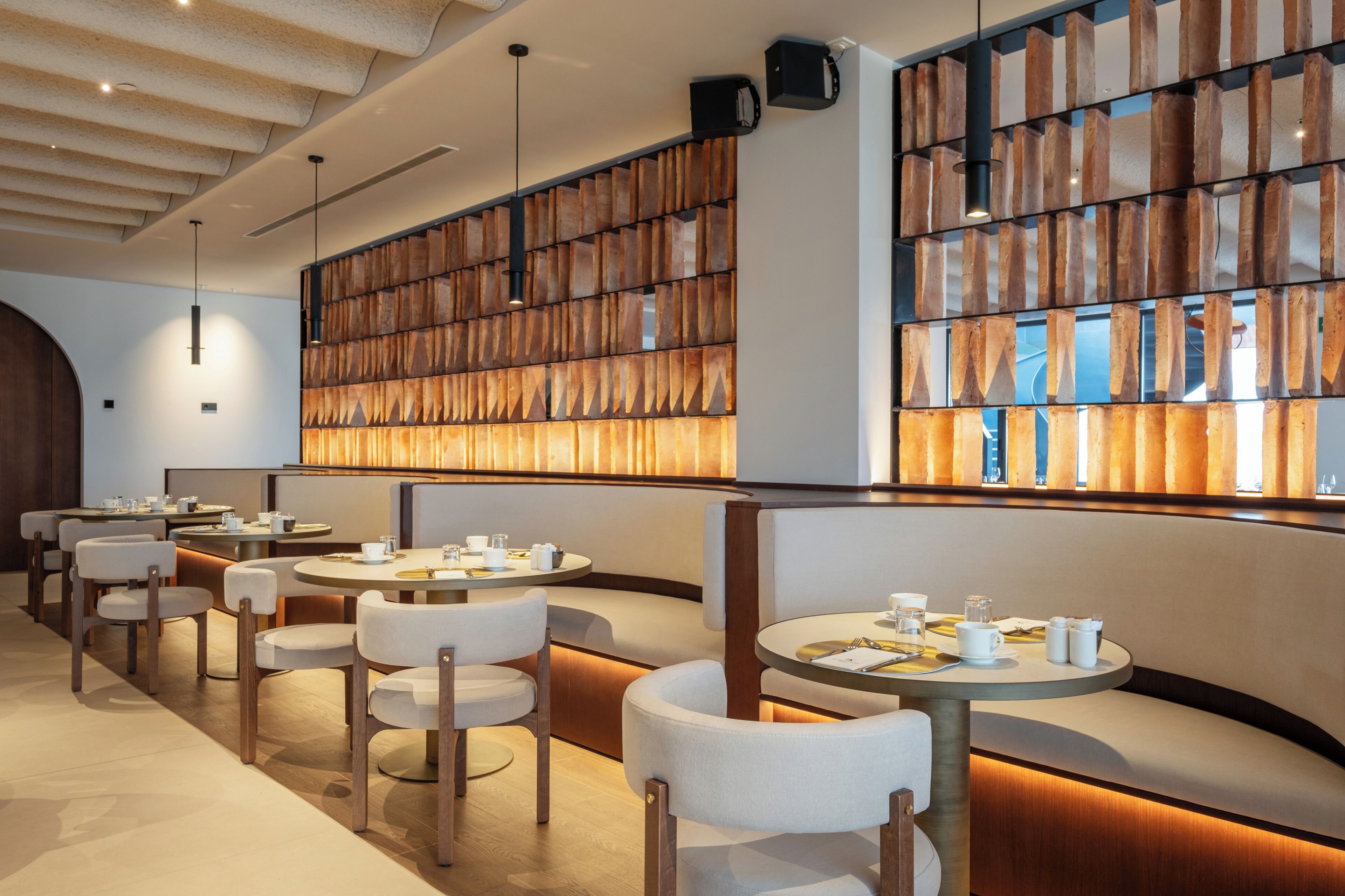 A modern restaurant with round tables, cushioned seating, and a wooden wall feature.