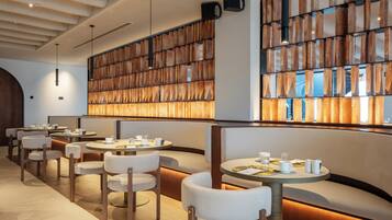 A modern restaurant with round tables, cushioned seating, and a wooden wall feature.