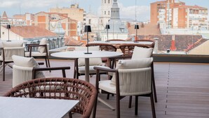 Terrassa al terrat amb mobles de vimet, una taula rodona i vista als edificis de la ciutat.