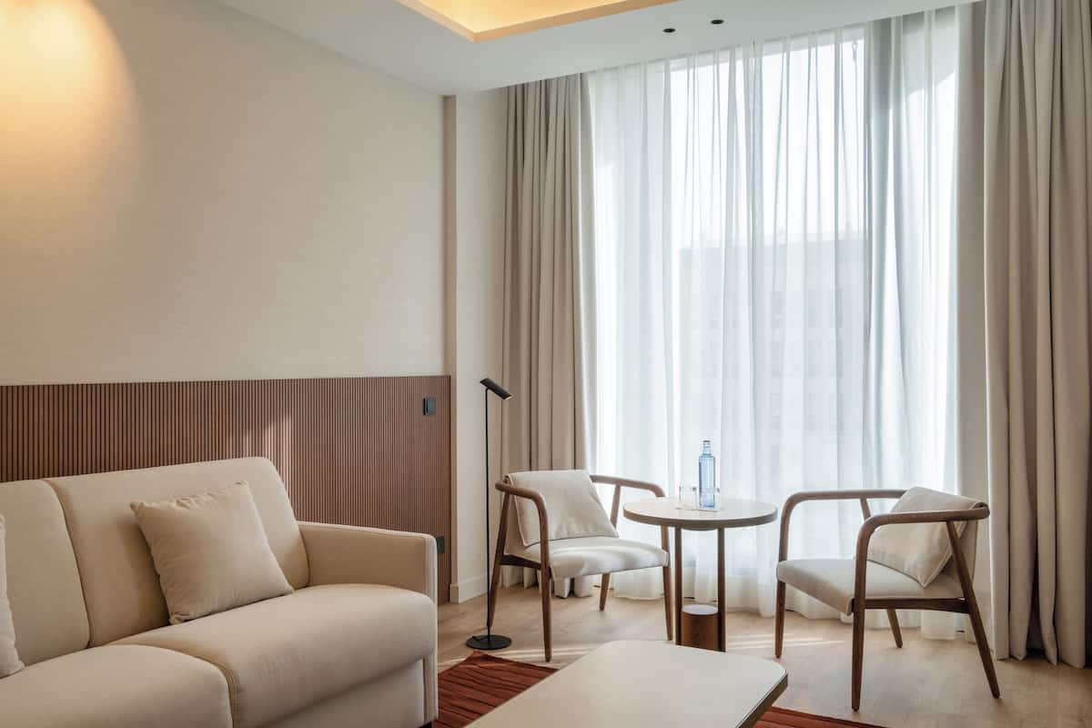 Une chambre d’hôtel moderne avec un canapé, deux fauteuils, une petite table et une lampe sur pied.
