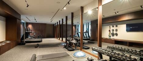 Un gimnasio con cintas de correr, bancos de pesas y mancuernas.