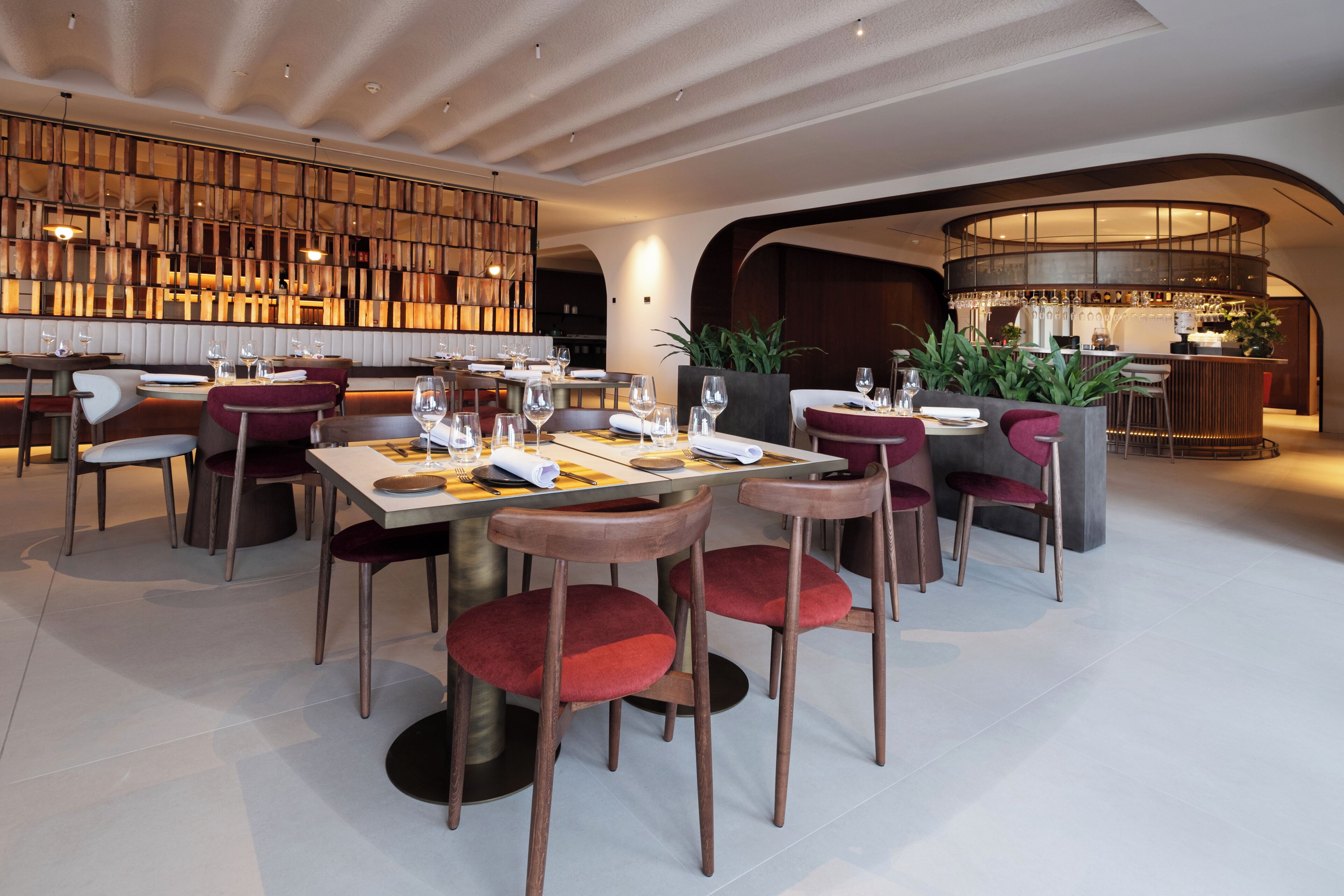 Ein modernes Restaurant mit Barbereich, Holzwand und rot gepolsterten Stühlen.