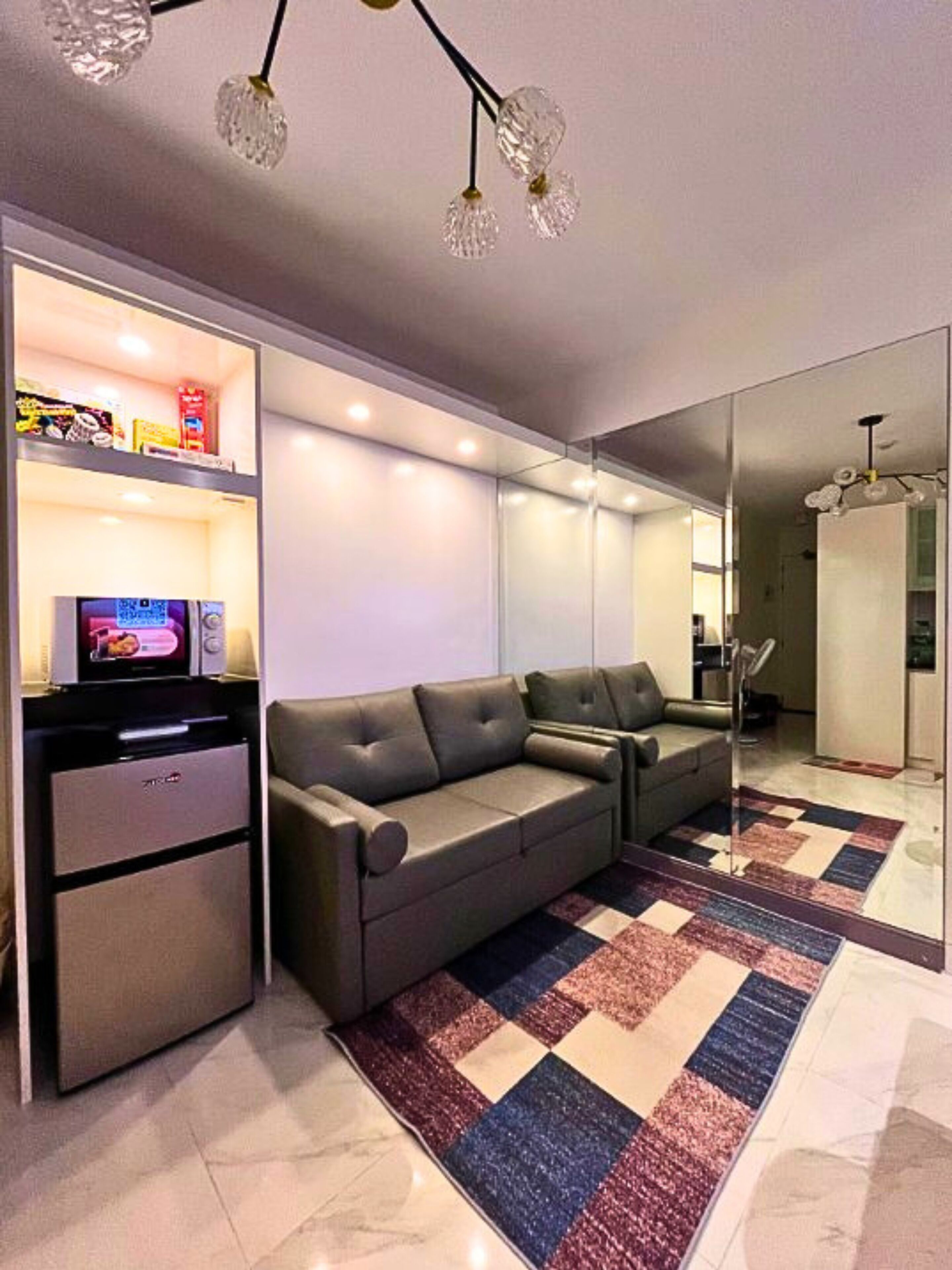 Un salon moderne comprenant un canapé, un téléviseur à écran plat, un petit réfrigérateur et un miroir.