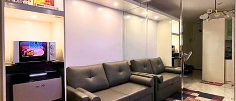 Un salon moderne comprenant un canapé, un téléviseur à écran plat, un petit réfrigérateur et un miroir.