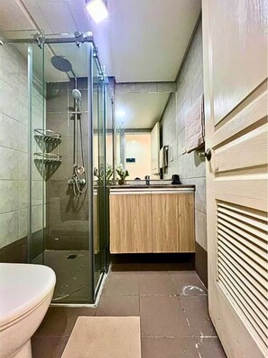 A bathroom with a glass-enclosed shower, a wooden vanity, and a toilet. - Stay Beside Mall of Asia Walk & Explore (Parañaque)