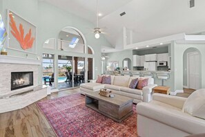 A spacious living room with a fireplace, a large sofa set, a coffee table, and a view of the outdoor patio. - Reel Relaxed | Team Joseph Ellen (Jacksonville Beach)