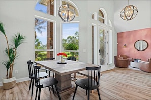 A dining area with a wooden table and chairs, large windows, and a view of greenery. - Reel Relaxed | Team Joseph Ellen (Jacksonville Beach)