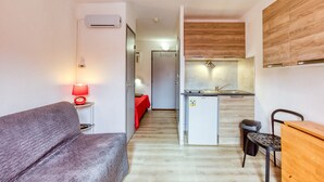 Un espacio habitable compacto con kitchenette, un sofá, una pequeña mesa de comedor y una lámpara roja.