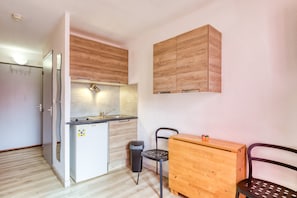 Une cuisine de taille réduite, équipée d’un réfrigérateur, d’un évier et de meubles de rangement en bois.