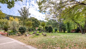 Un jardín con un sendero pavimentado, varios árboles y una zona verde.