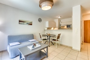 A living room with a sofa, a coffee table, a dining table with chairs, a kitchen area with cabinets and a microwave, and a wooden door.